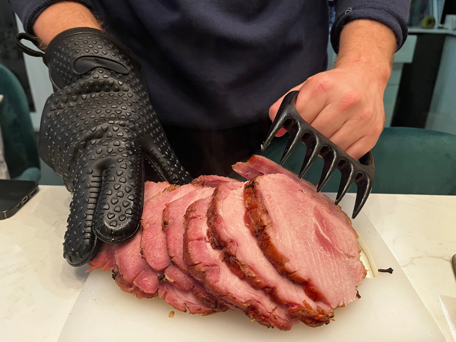 Man with Silicone Meat Gloves Preparing Sliced Pork Roast with Meat Claw in Other Hand